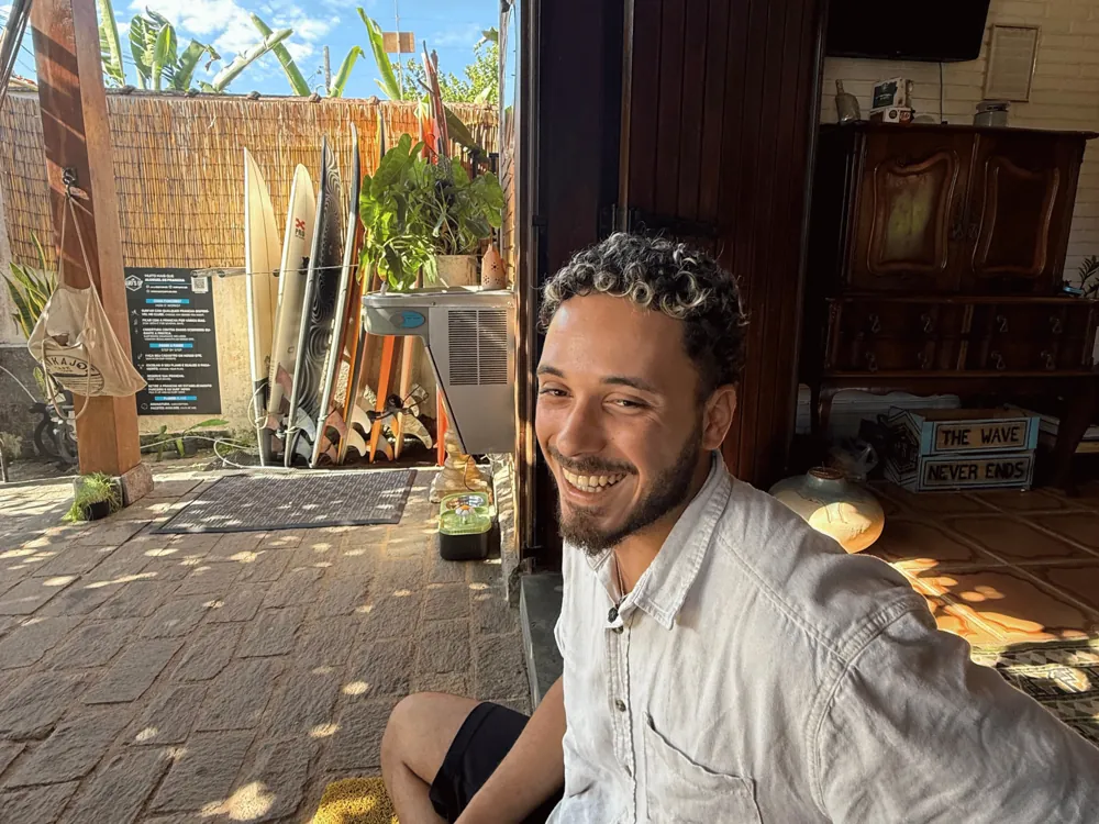 Hóspede sorrindo com as pranchas ao fundo