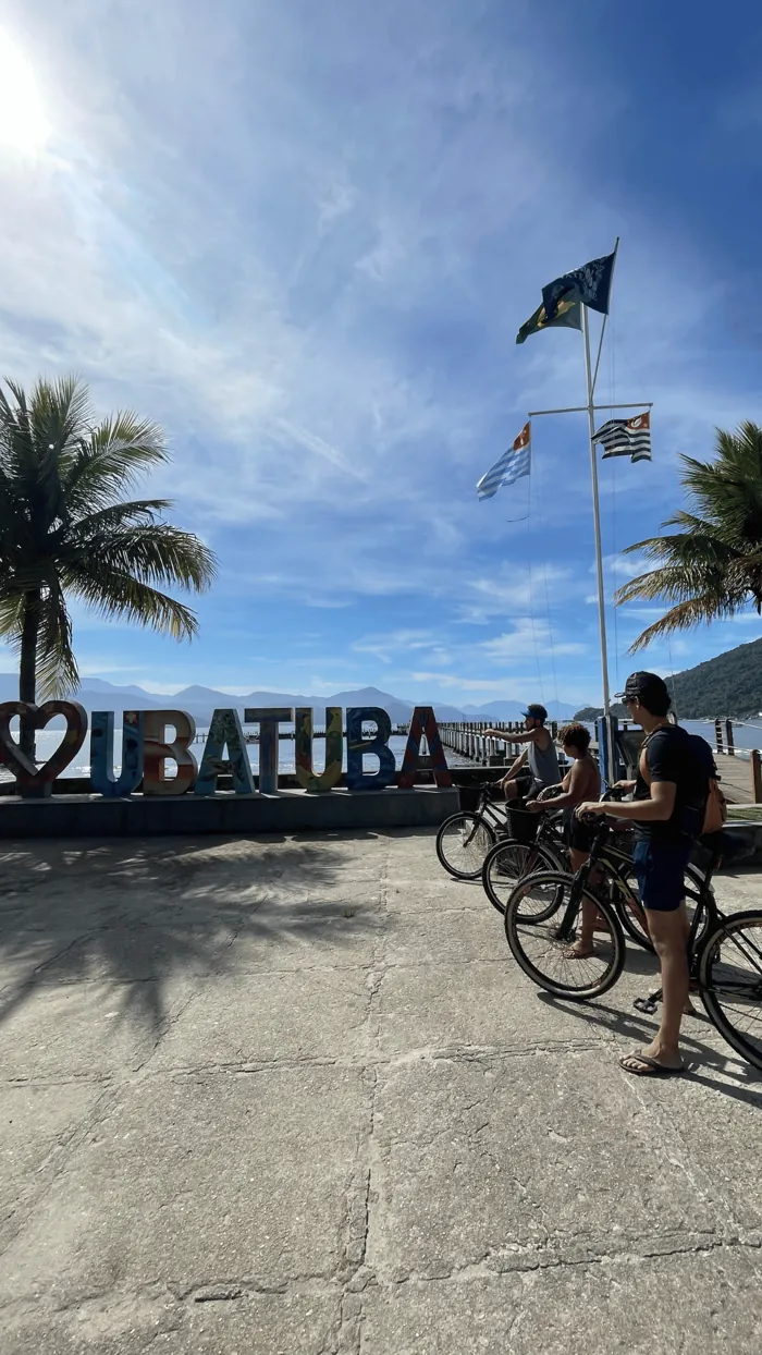 Letreiro de Ubatuba na orla, com bicicletas e palmeiras