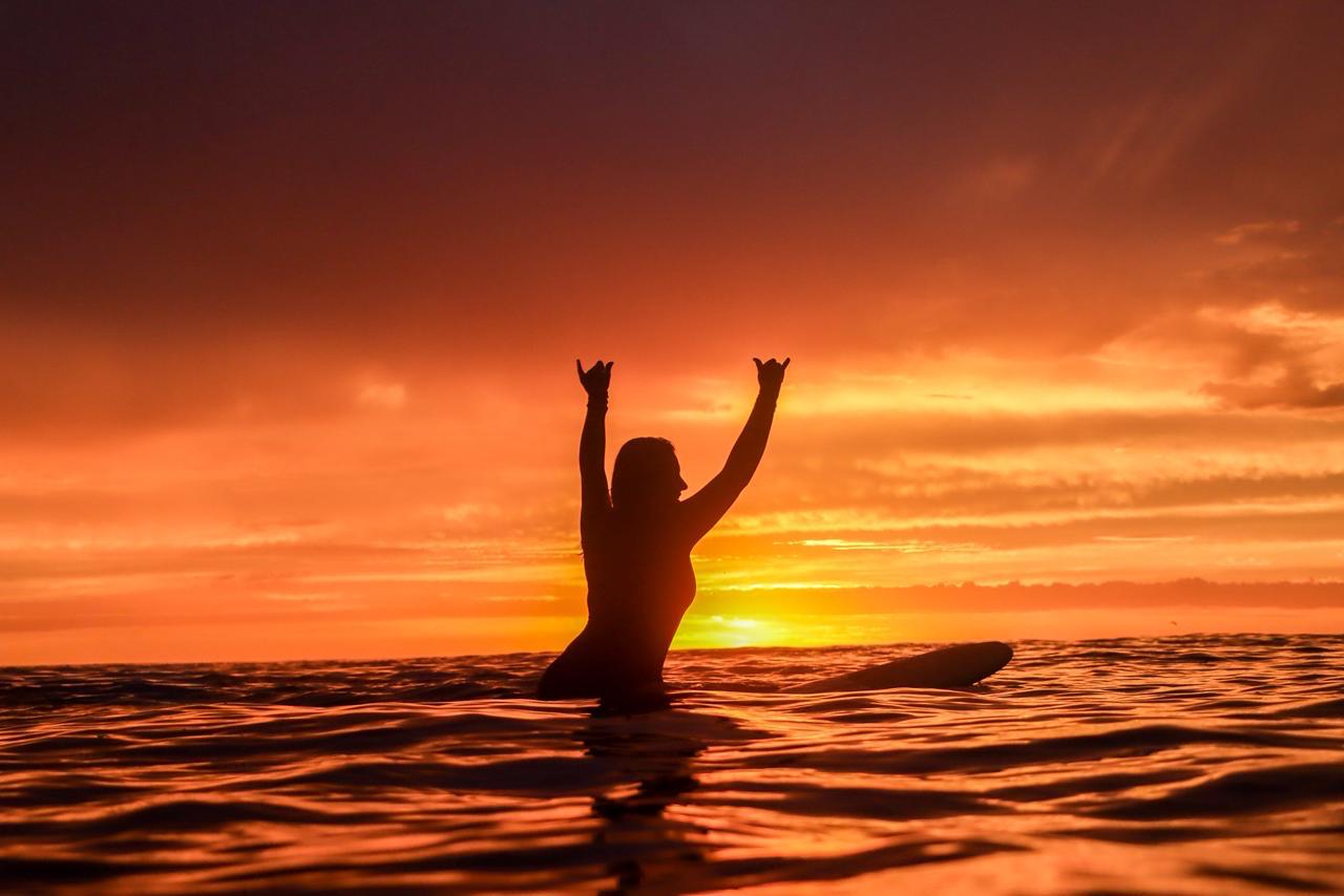 Surfista celebrando no mar ao nascer do sol
